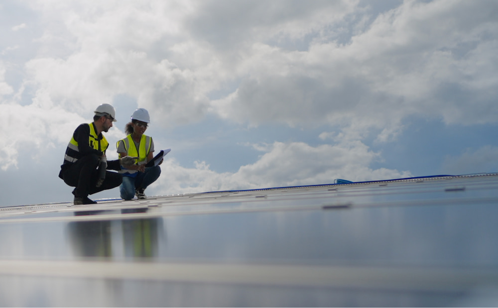 Professionals in safety vests examining a rooftop solar panel.