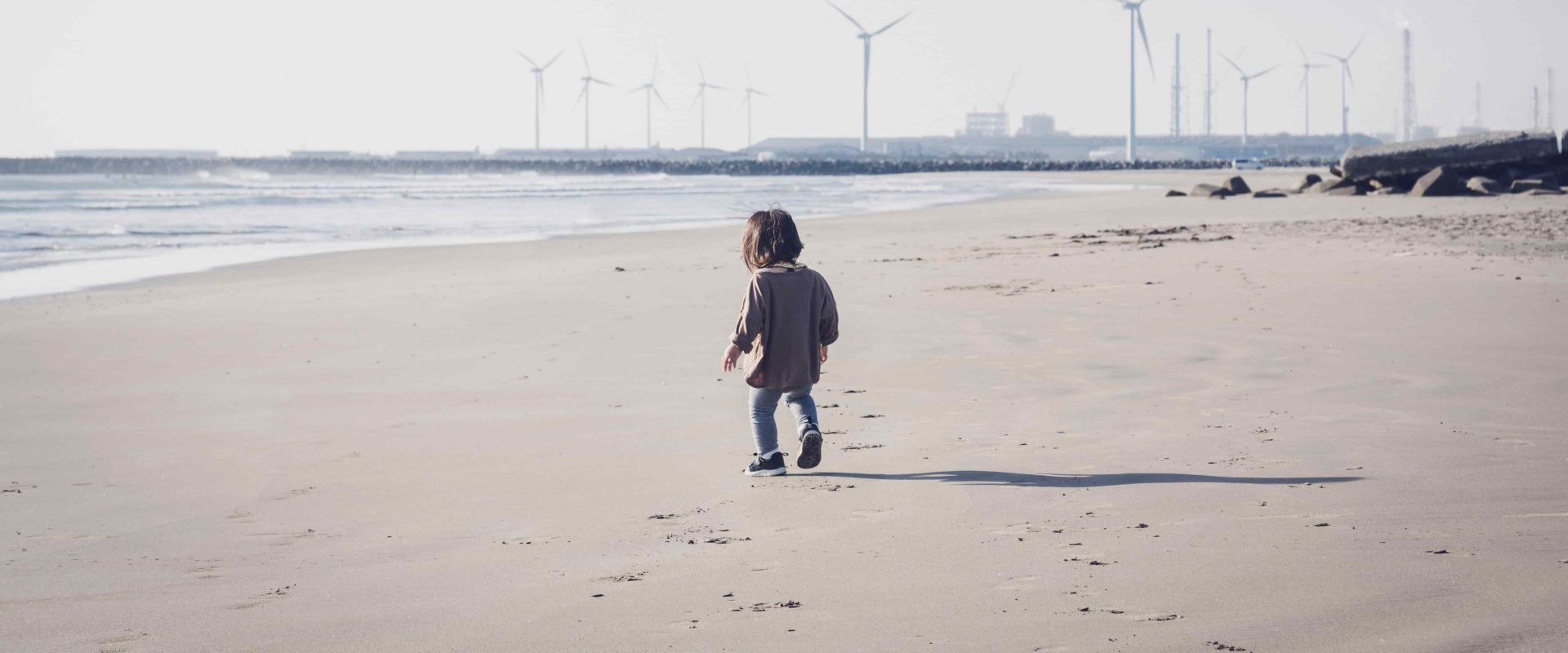 Child walking in the beach close to wind farm